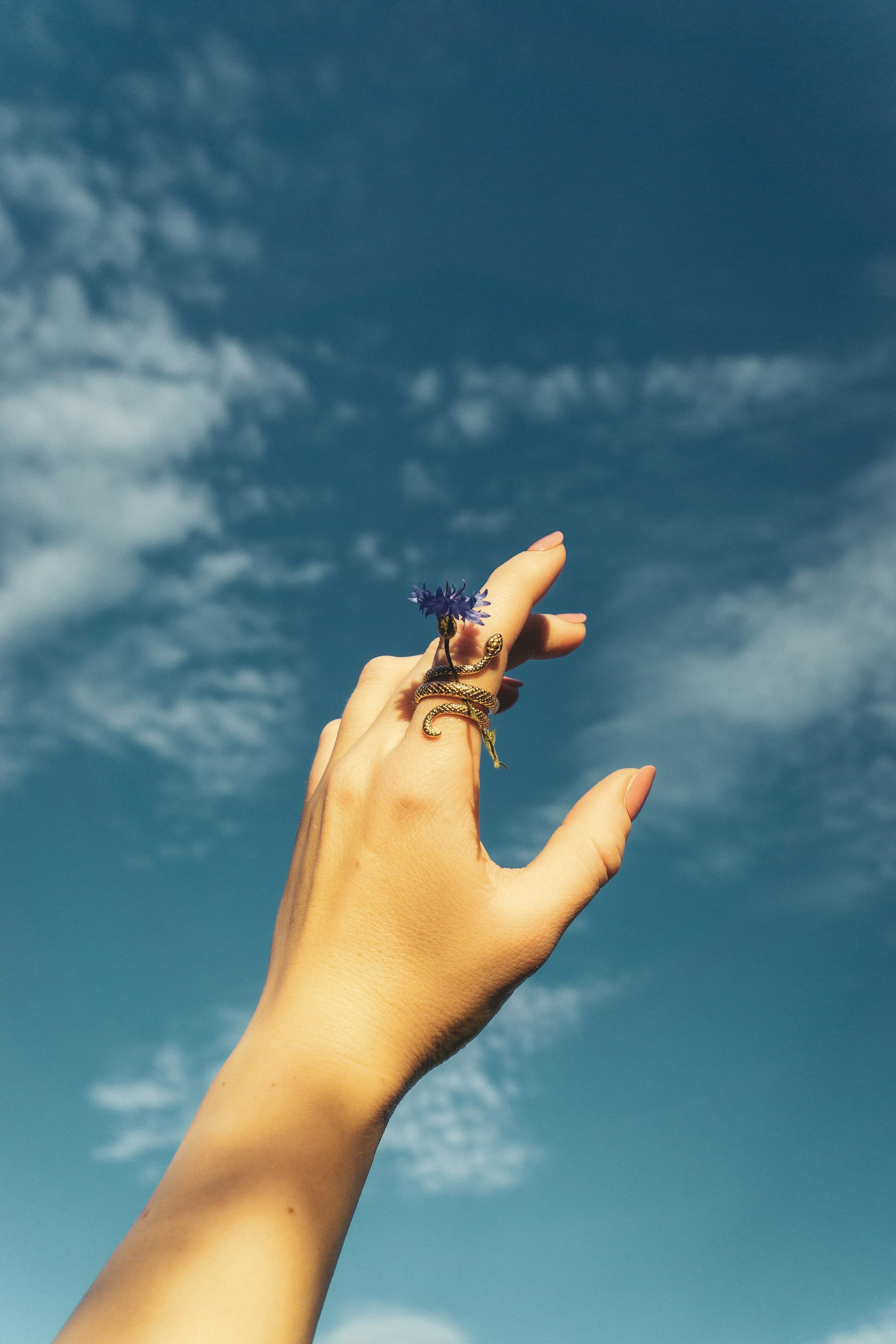 Person reaching out to a flying object under the clouds.