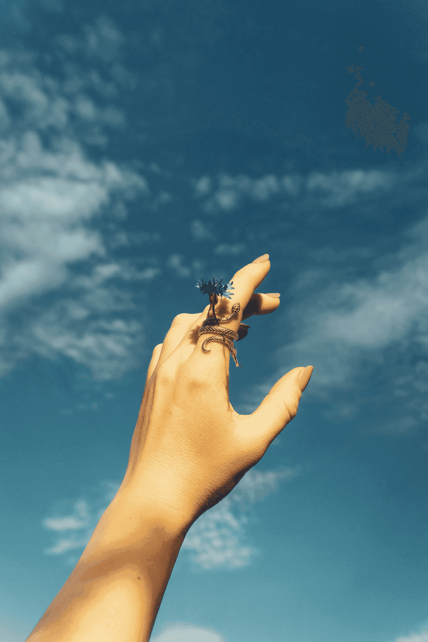 Person reaching out to a flying object under the clouds.
