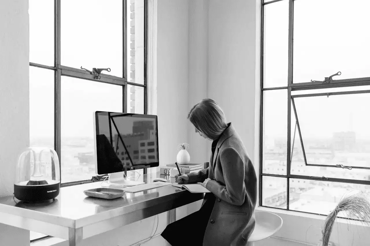 Schwarz-Weiß-Foto einer berufstätigen Frau, die an einem Schreibtisch mit Computer arbeitet