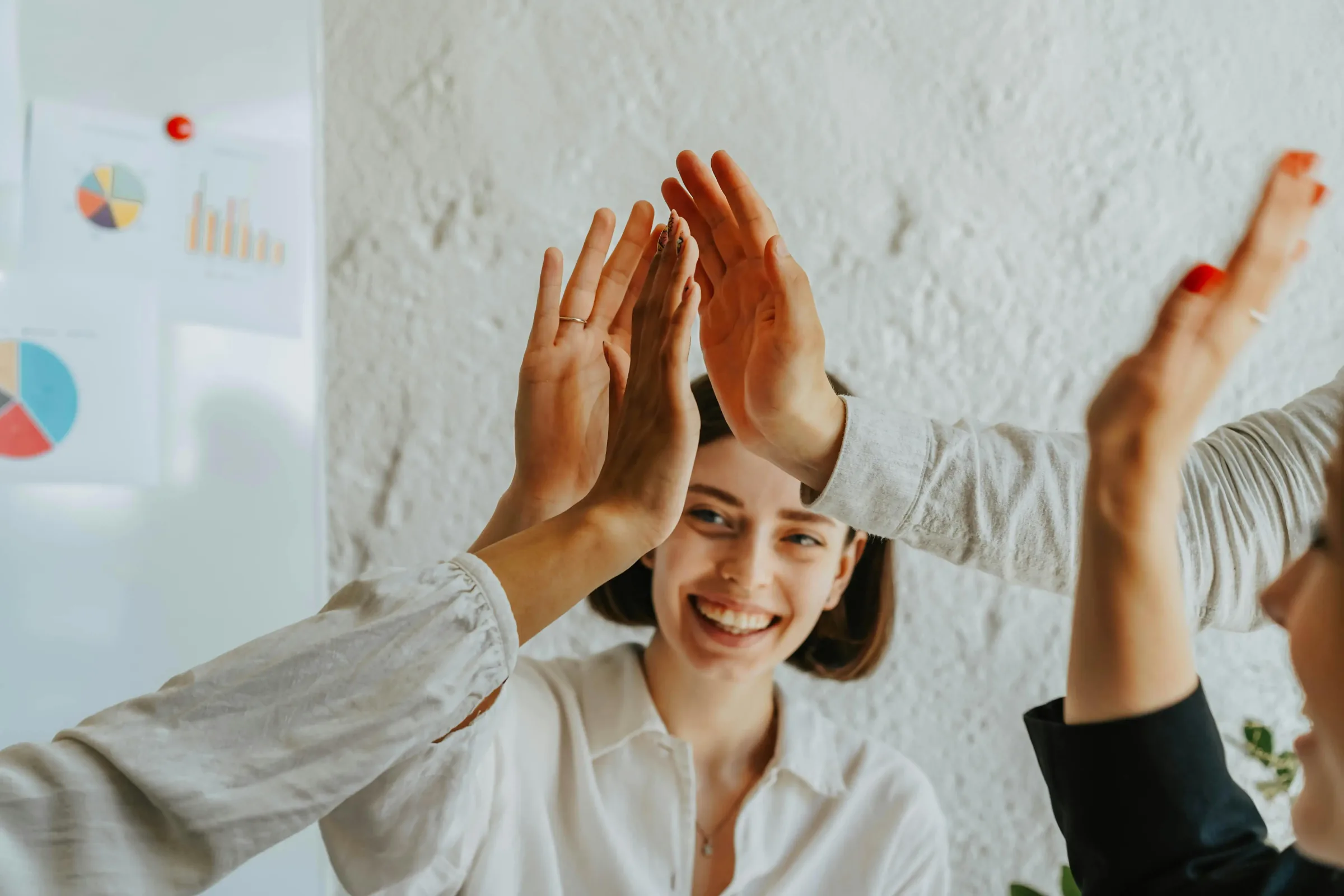 Zwei berufstätige Frauen lächeln und klatschen sich in einem Büro gegenseitig ab