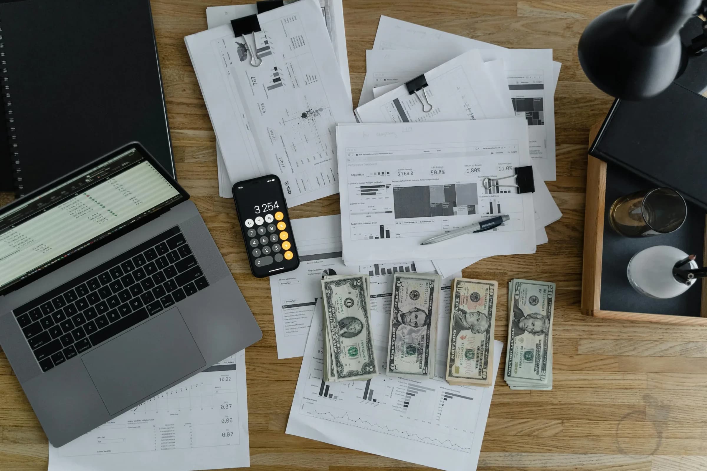 Draufsicht auf einen Schreibtisch mit Laptop, Taschenrechner, Bargeld und Finanzunterlagen