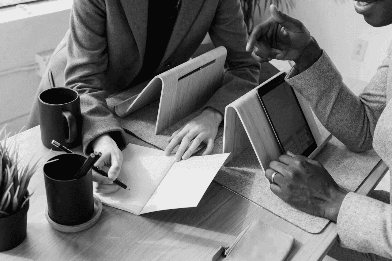 A top-down, black and white view of professionals collaborating over notebooks and a tablet to find financial RevOps solutions.