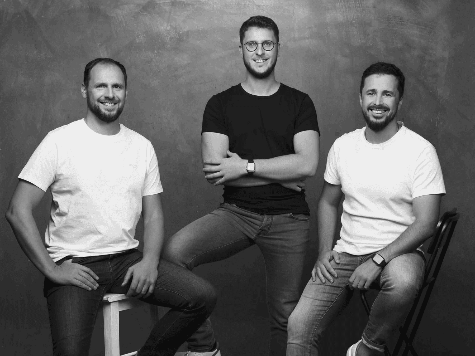 Three men posing together in a studio setting, wearing casual t-shirts and jeans for a professional team photo.
