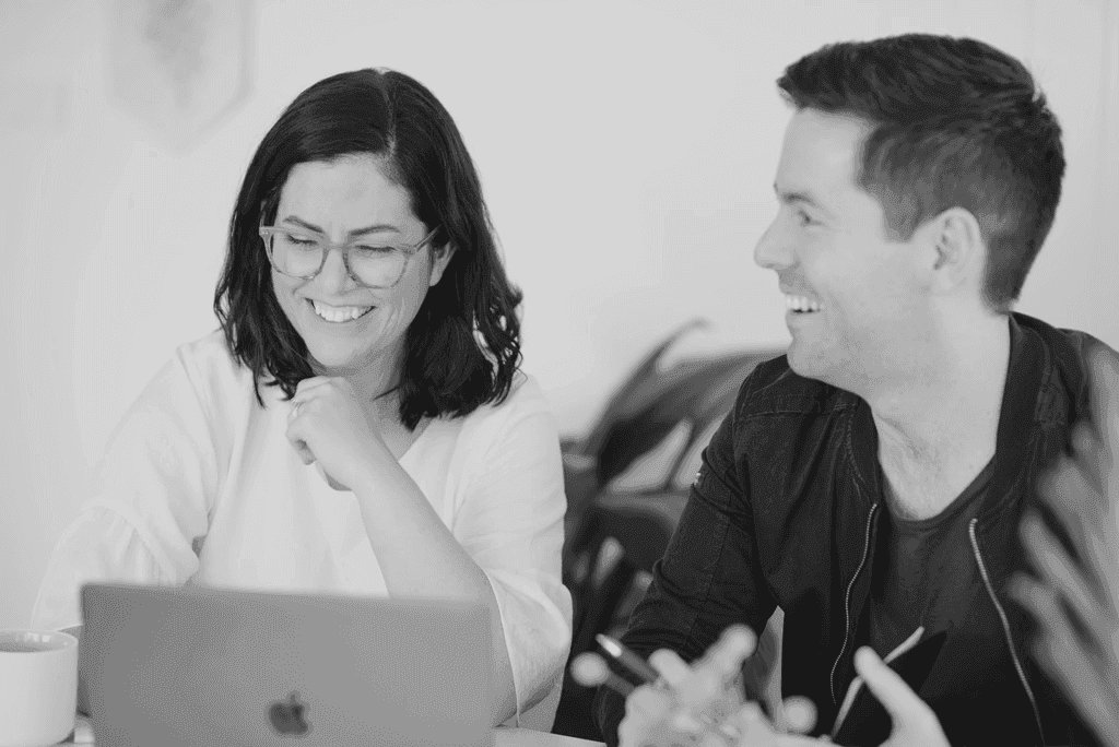 Ein Mann und eine Frau lachen, während sie gemeinsam auf einen Laptop schauen – ein freundlicher, kooperativer Arbeitsplatz.